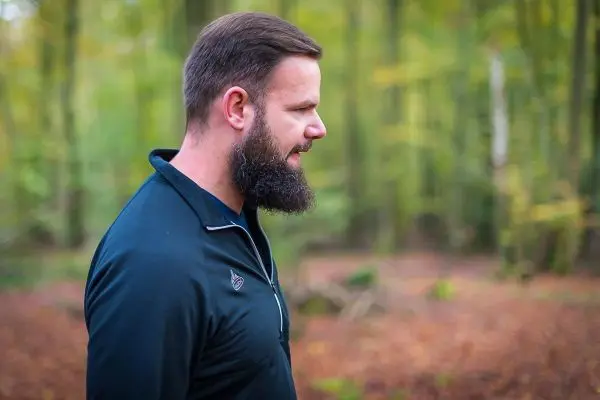 Mann mit Bart geht durch einen Wald mit herbstlichem Laub