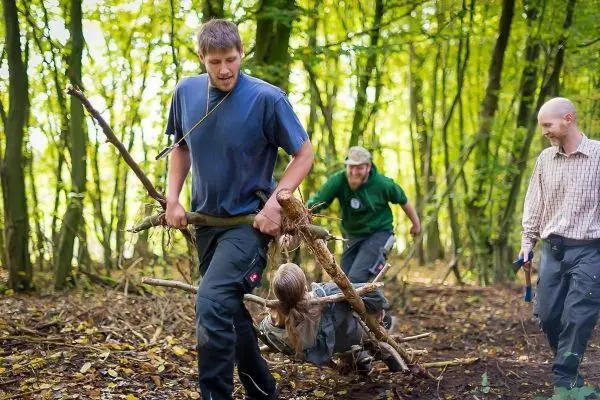 Mann trägt improvisierte Trage mit Kind durch den Wald