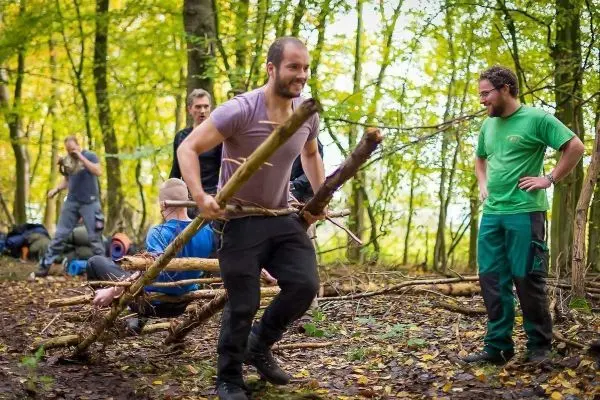 Mann trägt selbstgebaute Konstruktion aus Ästen durch den Wald