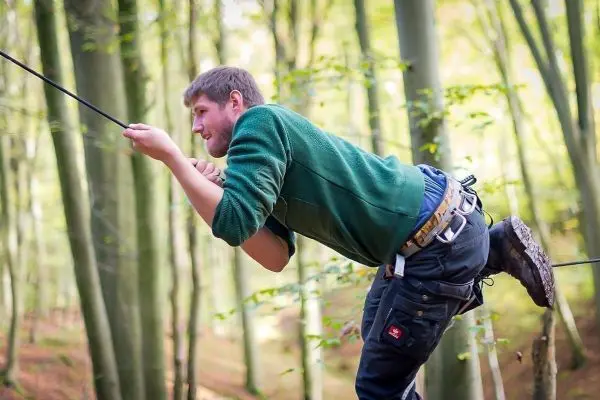 Mann überquert eine selbstgebaute Seilbrücke zwischen Bäumen