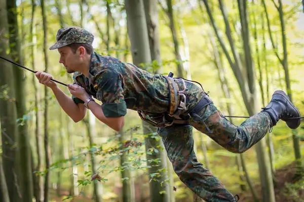 Mann überquert eine selbstgebaute Seilbrücke zwischen Bäumen