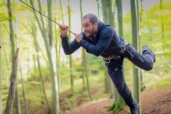 Mann überquert eine selbstgebaute Seilbrücke zwischen Bäumen
