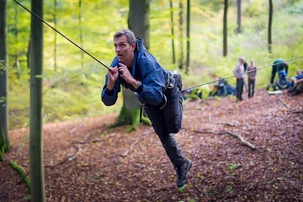 Mann überquert eine selbstgebaute Seilbrücke zwischen Bäumen im Wald