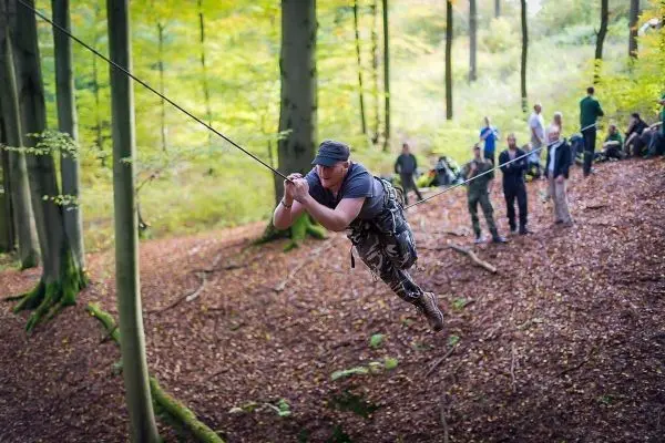 Mann überquert eine selbstgebaute Seilbrücke zwischen Bäumen im Wald