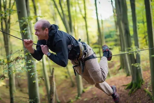 Mann überquert selbstgebaute Seilbrücke zwischen Bäumen im Wald