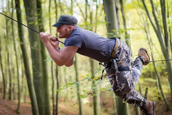 Mann überquert selbstgebaute Seilbrücke zwischen Bäumen im Wald