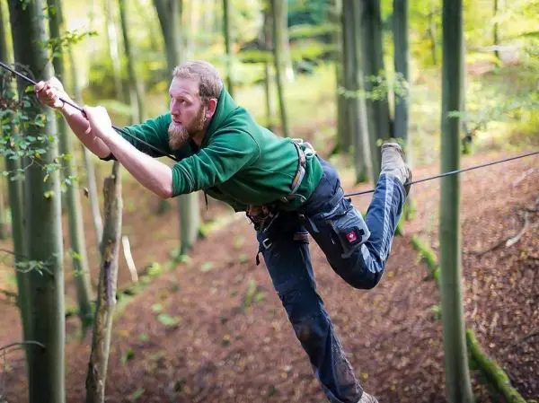 Mann überquert selbstgebaute Seilbrücke zwischen Bäumen im Wald