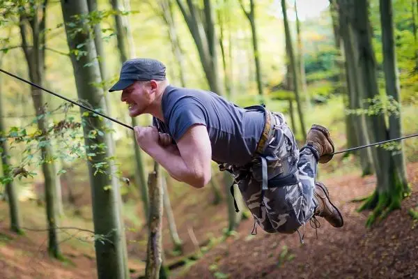 Mann überquert selbstgebaute Seilbrücke zwischen Bäumen im Wald