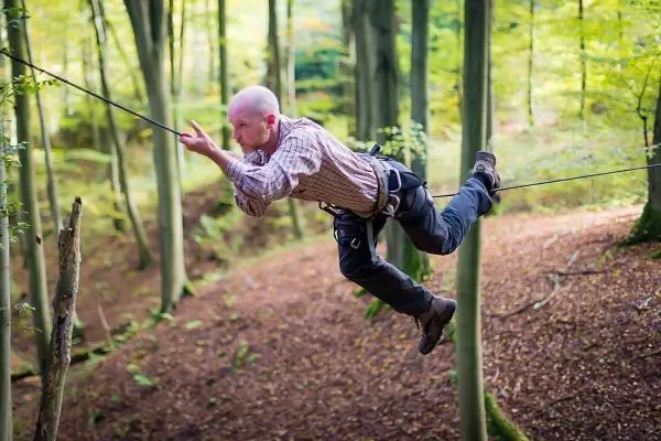 Mann überquert selbstgebaute Seilbrücke zwischen Bäumen im Wald