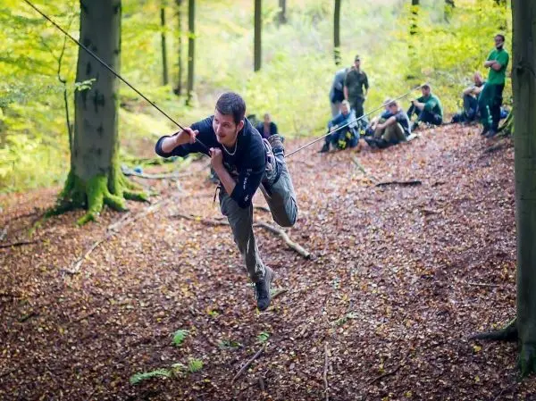 Mann überquert selbstgebaute Seilbrücke zwischen Bäumen im Wald
