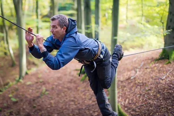 Mann überquert selbstgebaute Seilbrücke zwischen Bäumen im Wald