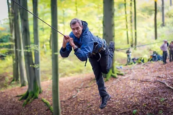 Mann überquert selbstgebaute Seilbrücke zwischen Bäumen im Wald