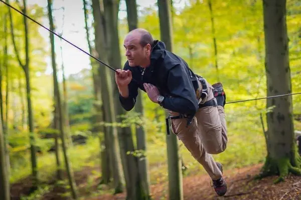 Mann überquert selbstgebaute Seilbrücke zwischen Bäumen im Wald