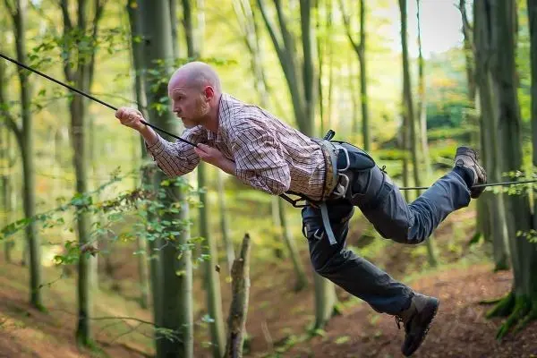 Mann überquert selbstgebaute Seilbrücke zwischen Bäumen im Wald