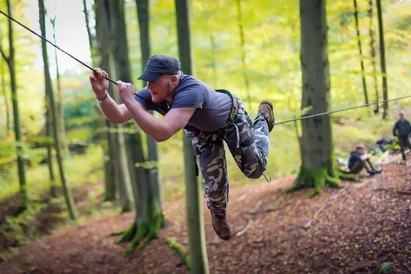 Mann überquert selbstgebaute Seilbrücke zwischen Bäumen im Wald