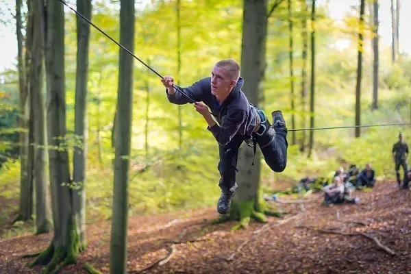Mann überquert selbstgebaute Seilbrücke zwischen Bäumen im Wald