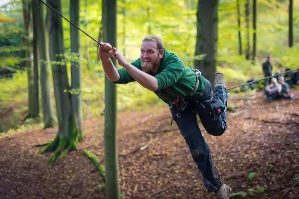 Mann überquert selbstgebaute Seilbrücke zwischen Bäumen im Wald