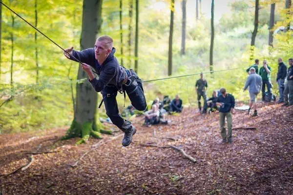 Mann überquert selbstgebaute Seilbrücke zwischen Bäumen im Wald