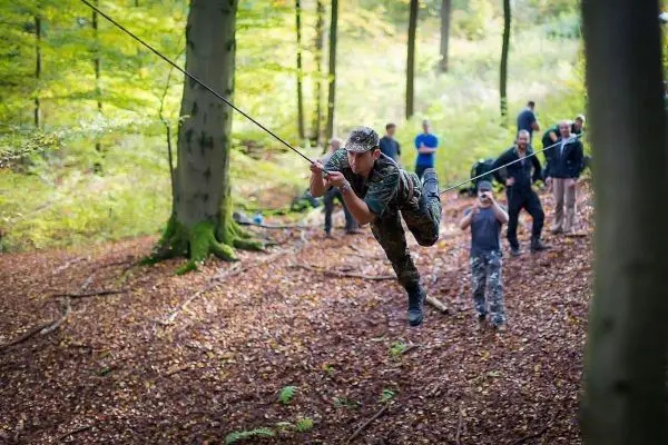 Mann überquert selbstgebaute Seilbrücke zwischen Bäumen im Wald