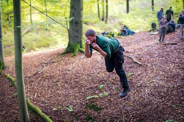 Mann überquert selbstgebaute Seilbrücke zwischen Bäumen im Wald