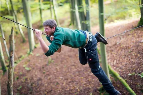 Mann überquert selbstgebaute Seilbrücke zwischen Bäumen im Wald