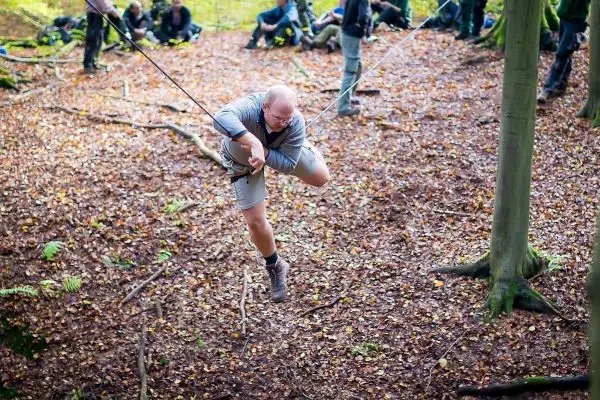 Mann überquert selbstgebaute Seilbrücke zwischen zwei Bäumen im Wald