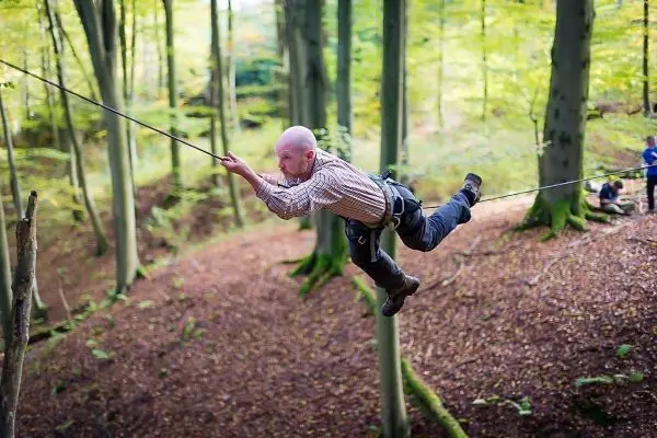 Mann überquert selbstgebaute Seilbrücke zwischen zwei Bäumen im Wald