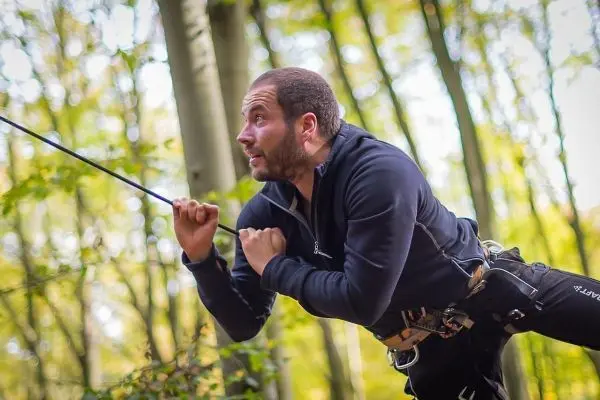 Mann zieht an einem Seil während einer Seilquerung im Wald