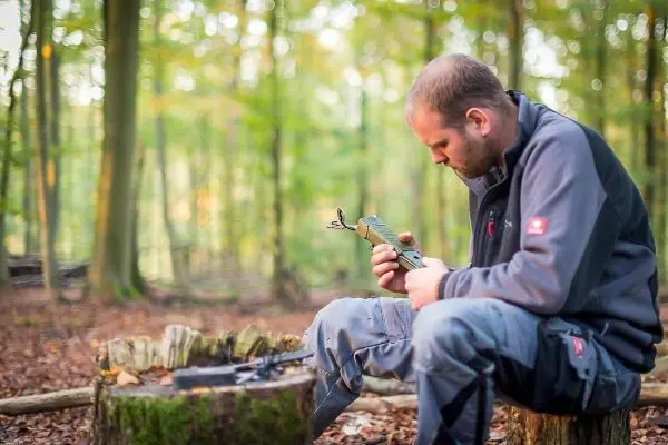 Messer wird auf einem Holzstück im Wald bearbeitet
