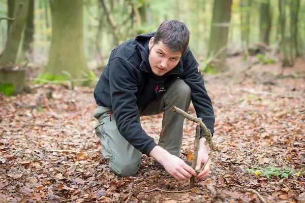 Person baut eine Falle aus Ästen im Wald beim Survival Training