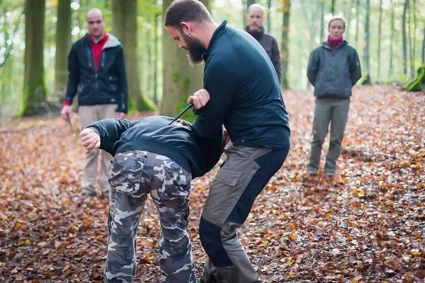 Person demonstriert eine Technik zur Kontrolle einer anderen Person im Wald
