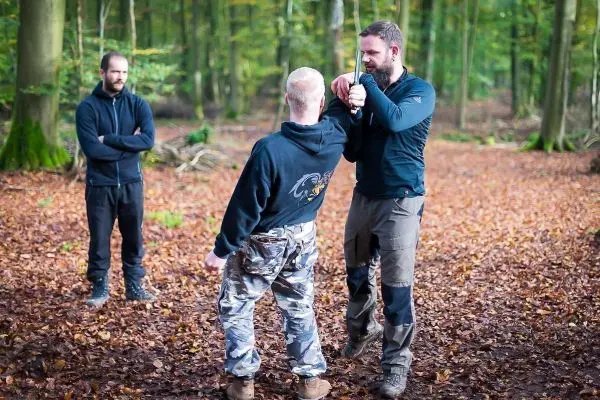 Person demonstriert Technik an anderer Person im Wald beim Survival Training