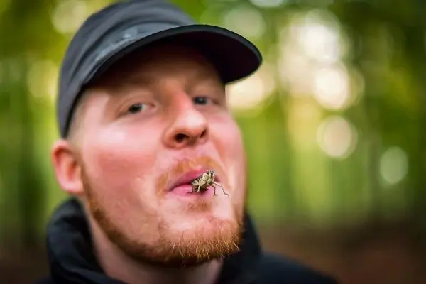 Person hält eine Heuschrecke zwischen den Lippen