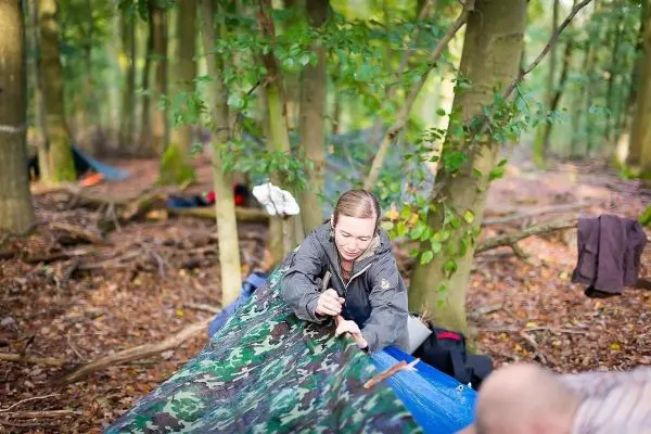 Person spannt eine Plane zwischen Bäumen im Wald beim Überlebenstraining
