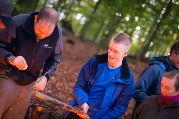Person zeigt einem anderen, wie man einen Stock bearbeitet beim Survival Training