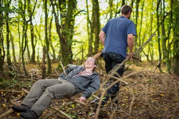 Person zieht andere Person auf einer improvisierten Trage durch den Wald