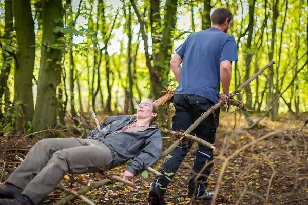 Person zieht andere Person auf einer selbstgebauten Trage durch den Wald