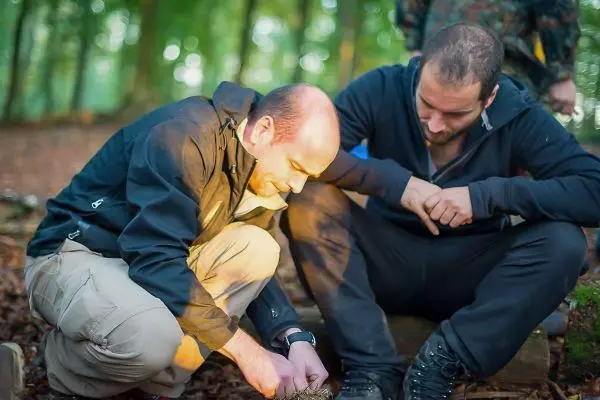 Person zündet Feuerstelle an, während andere zuschaut