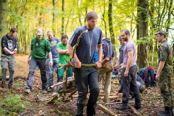 Teilnehmer tragen selbstgebaute Trage mit Holzstücken durch den Wald