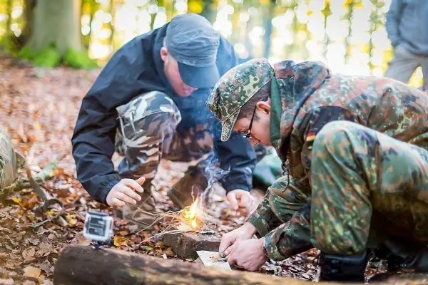 Zunder glimmt auf einem Holzstück, während zwei Personen darüber gebeugt sind