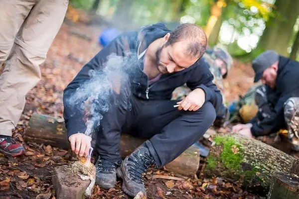 Zunder glimmt, während ein Mann mit zwei Stäben Funken erzeugt