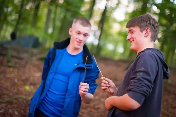 Zwei Jugendliche halten jeweils einen Stock in der Hand und lächeln