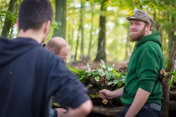 Zwei Personen arbeiten an einer Holzstruktur im Wald, eine Person lächelt