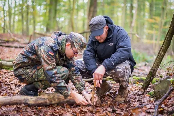 Zwei Personen bauen eine Holzstruktur im Wald aus Ästen und Zweigen