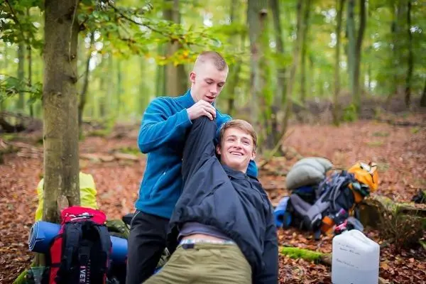 Zwei Personen helfen sich gegenseitig beim Anziehen einer Jacke im Wald