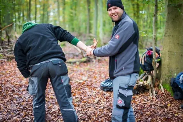Zwei Personen in Waldumgebung, eine Person hält die Hand des anderen
