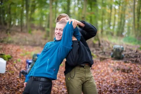 Zwei Personen interagieren spielerisch im Wald, umgeben von Laub und Rucksäcken
