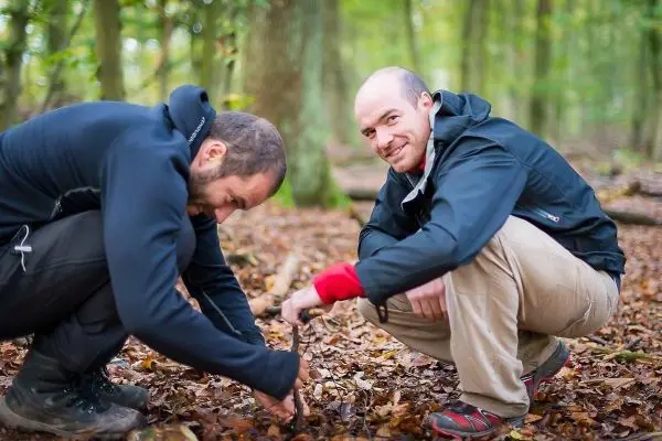 Zwei Personen knien im Laub und arbeiten an einer Holzstruktur