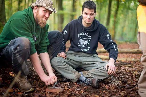 Zwei Personen sitzen im Laub und bearbeiten einen Stein mit einem Messer