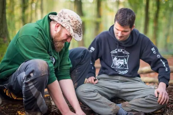 Zwei Personen sitzen im Wald und arbeiten an einer Holzstruktur